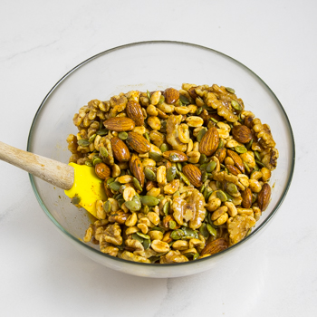 Glass mixing bowl full of mixed nuts with a small spatula