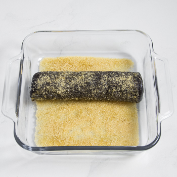 A log of dark dough in a glass baking dish lined with sanding or turbinado sugar